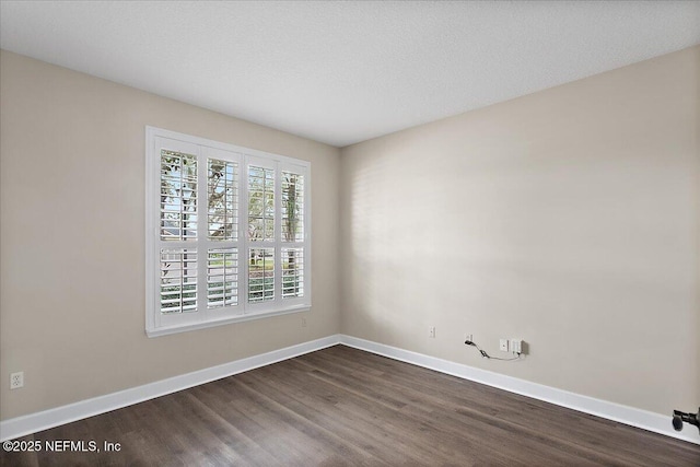 spare room with a textured ceiling, dark wood finished floors, and baseboards