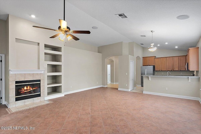 unfurnished living room featuring arched walkways, built in shelves, a textured ceiling, and a tile fireplace