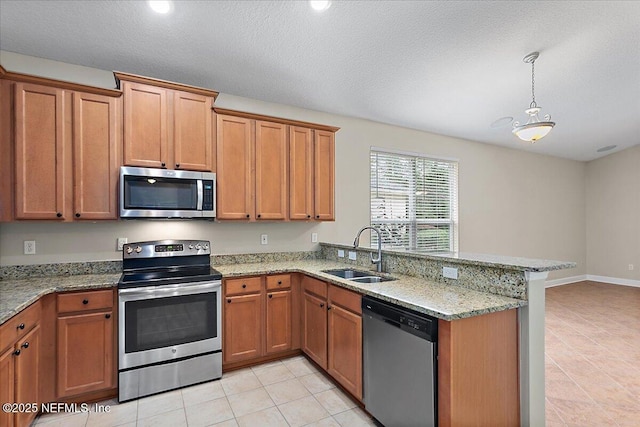 kitchen with brown cabinetry, light stone counters, a peninsula, stainless steel appliances, and a sink