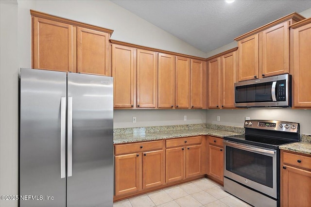 kitchen featuring light stone counters, lofted ceiling, appliances with stainless steel finishes, light tile patterned flooring, and a textured ceiling