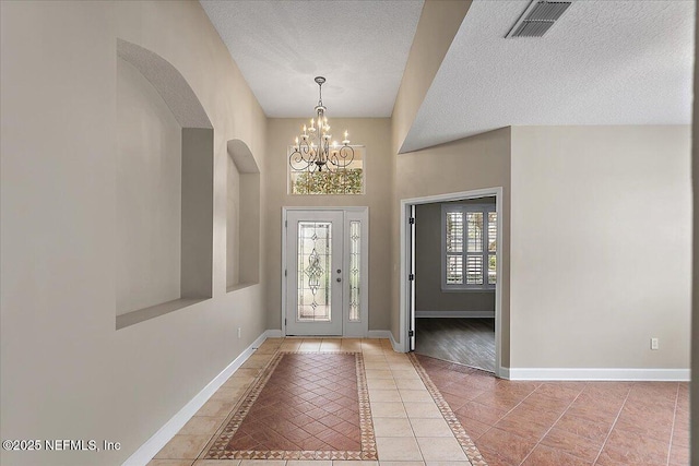 entryway with a notable chandelier, light tile patterned floors, visible vents, a textured ceiling, and baseboards