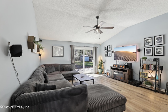 living area with a ceiling fan, a textured ceiling, a glass covered fireplace, wood finished floors, and vaulted ceiling