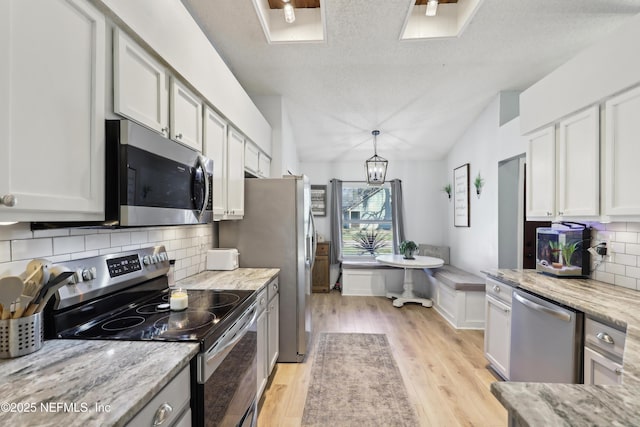 kitchen with light stone countertops, breakfast area, lofted ceiling, light wood-style flooring, and appliances with stainless steel finishes