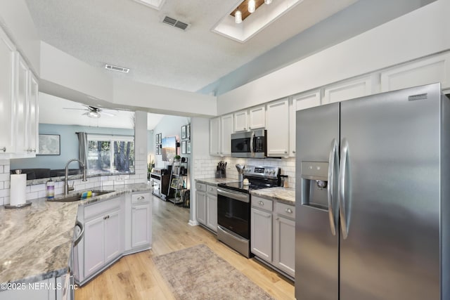 kitchen featuring visible vents, backsplash, light wood-style floors, stainless steel appliances, and a sink