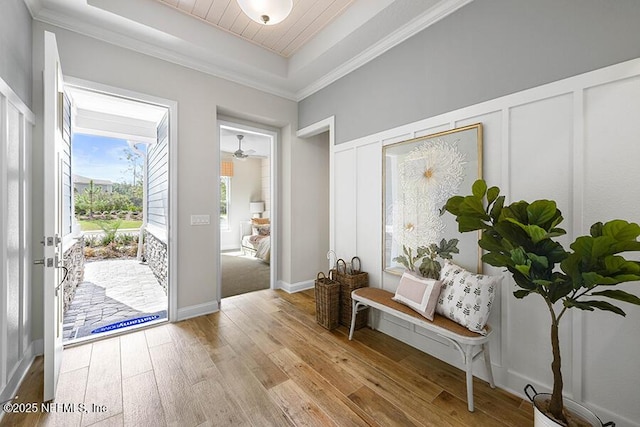 foyer with a tray ceiling, a decorative wall, light wood-style floors, and ornamental molding