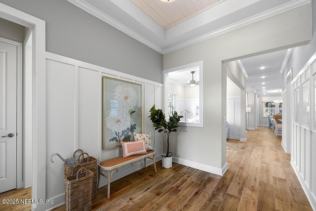 hall with wainscoting, light wood-style flooring, ornamental molding, and a decorative wall