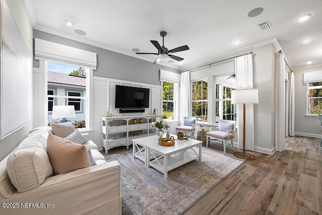 living area with plenty of natural light, wood finished floors, visible vents, and ornamental molding