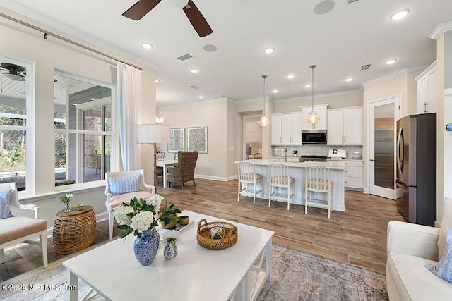 living area with ceiling fan, crown molding, visible vents, and light wood-type flooring