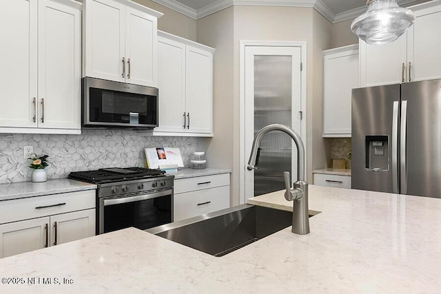 kitchen with a sink, light stone counters, appliances with stainless steel finishes, and crown molding