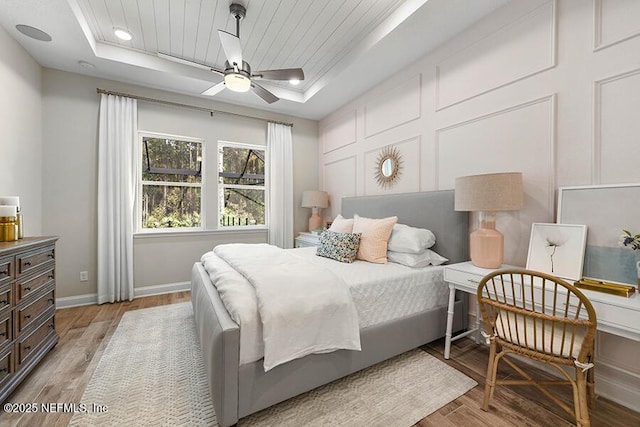 bedroom with baseboards, a raised ceiling, and light wood-style floors