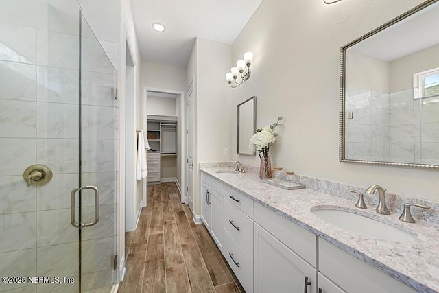 full bath with wood finish floors, a sink, a shower stall, double vanity, and a spacious closet