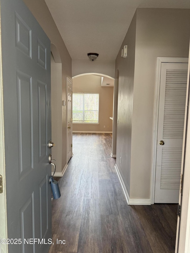 corridor featuring arched walkways, wood finished floors, and baseboards