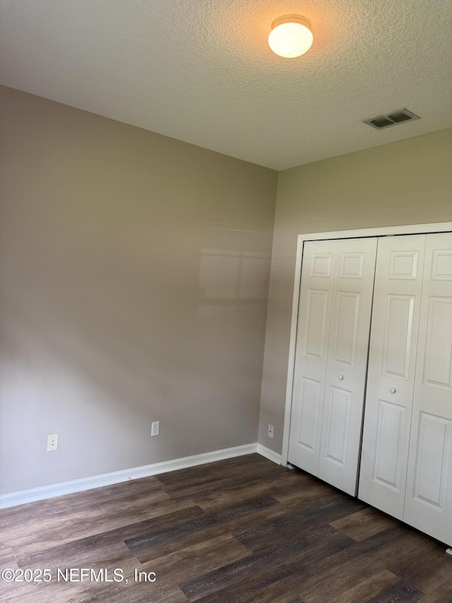 unfurnished bedroom featuring a textured ceiling, dark wood-type flooring, visible vents, baseboards, and a closet