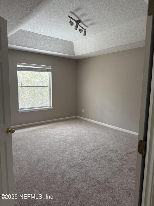 carpeted empty room with track lighting, a textured ceiling, and baseboards