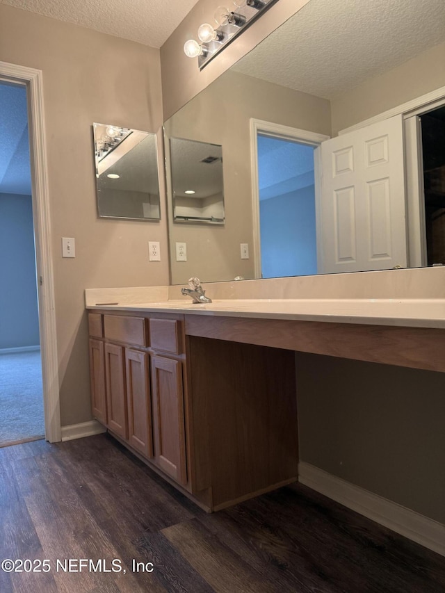 bathroom with a textured ceiling, wood finished floors, vanity, and baseboards