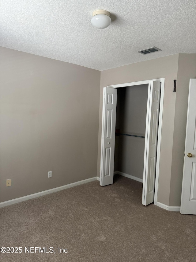 unfurnished bedroom with baseboards, visible vents, carpet, a textured ceiling, and a closet