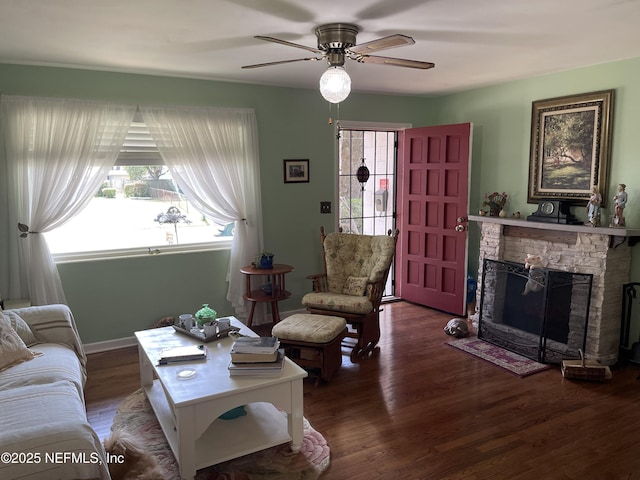 living area with a ceiling fan, a stone fireplace, and wood finished floors