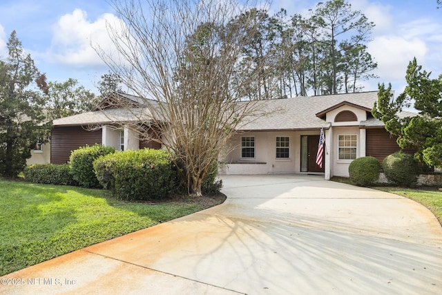 ranch-style house featuring roof with shingles, a front lawn, concrete driveway, and stucco siding