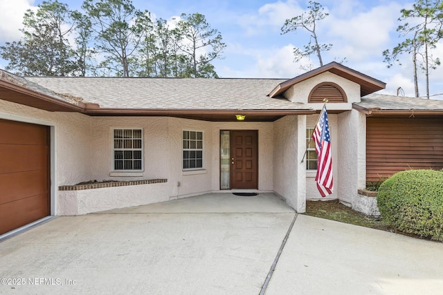 doorway to property with a garage, concrete driveway, a shingled roof, and stucco siding