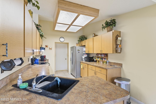 kitchen with freestanding refrigerator, black microwave, a sink, and light brown cabinetry