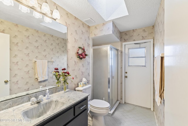 bathroom featuring toilet, vanity, a shower stall, a textured ceiling, and wallpapered walls