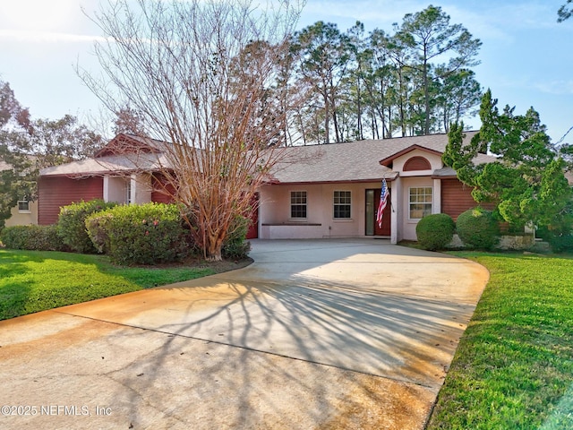 ranch-style home featuring driveway, roof with shingles, a front yard, and stucco siding