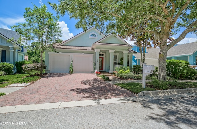 neoclassical / greek revival house with a porch, decorative driveway, a garage, and stucco siding