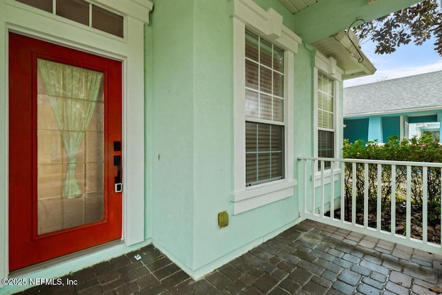 view of exterior entry with stucco siding and a porch