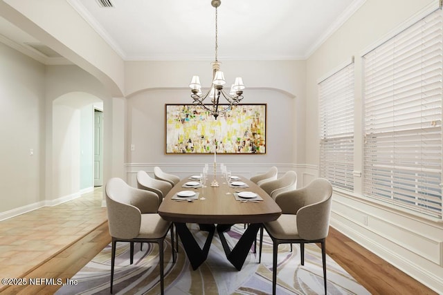 dining room with a notable chandelier, wood finished floors, arched walkways, crown molding, and baseboards