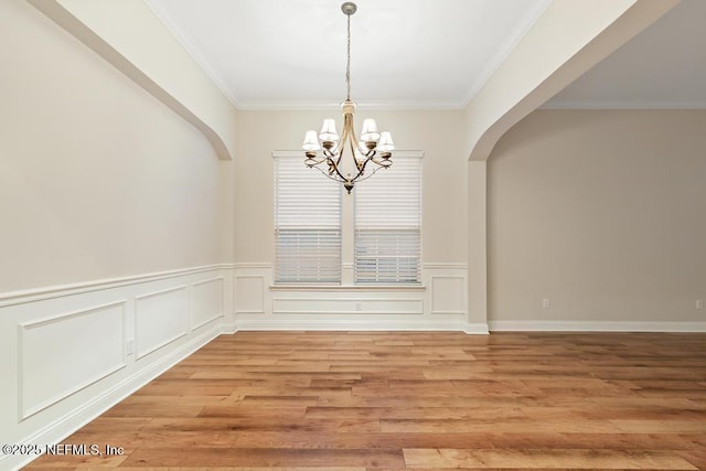 unfurnished dining area featuring a decorative wall, a notable chandelier, light wood-style flooring, and crown molding