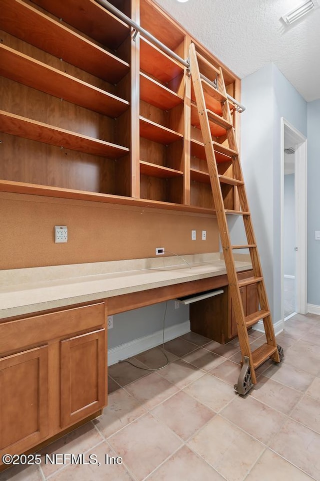 unfurnished office with baseboards, visible vents, built in desk, and a textured ceiling