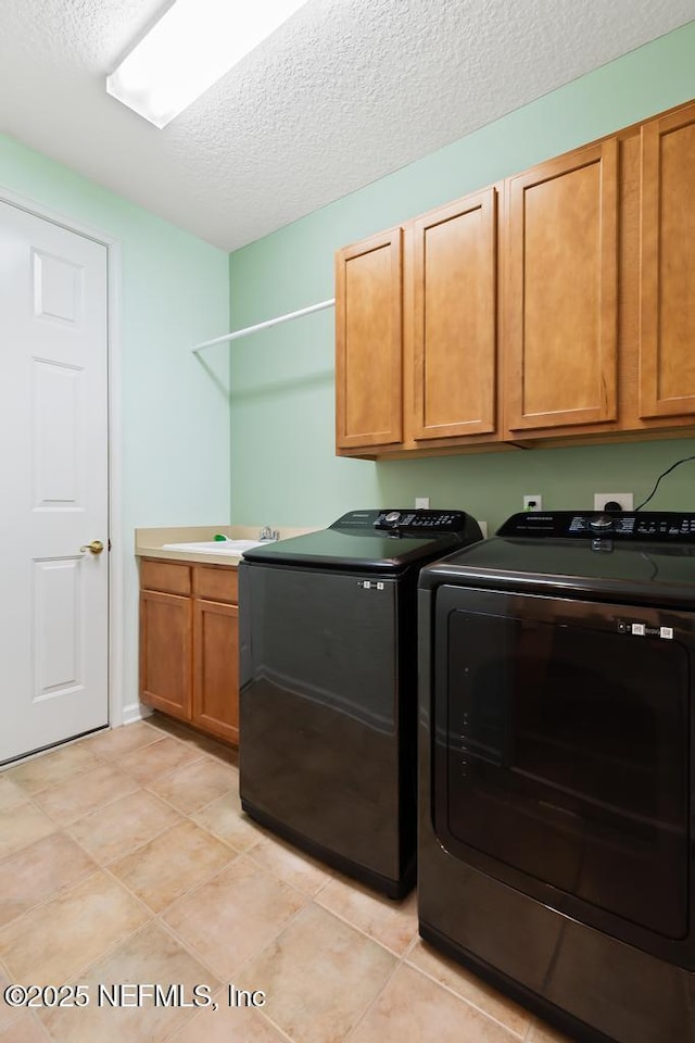 washroom featuring a sink, a textured ceiling, washing machine and dryer, cabinet space, and light tile patterned floors