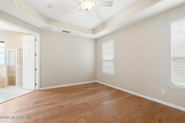 unfurnished room with light wood-type flooring, visible vents, a ceiling fan, a tray ceiling, and baseboards