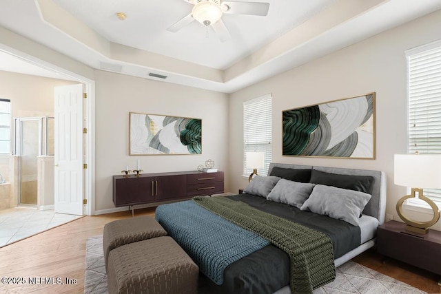 bedroom featuring visible vents, connected bathroom, ceiling fan, light wood-style floors, and a raised ceiling