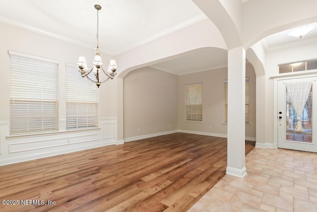 unfurnished dining area featuring light wood-style flooring, ornamental molding, arched walkways, an inviting chandelier, and baseboards