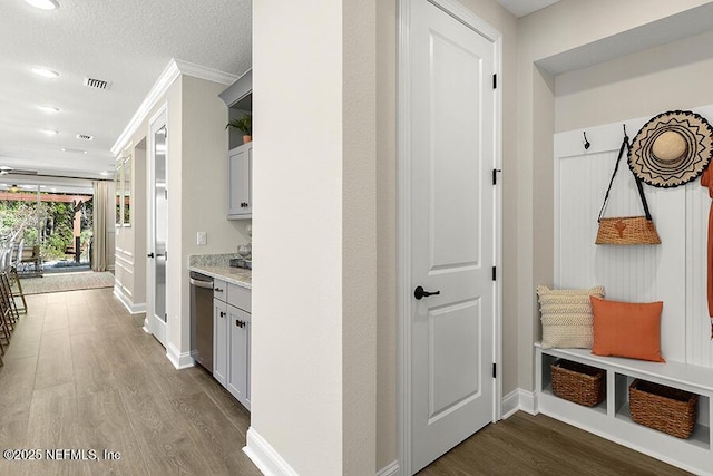 mudroom with visible vents, a textured ceiling, crown molding, baseboards, and dark wood-style flooring