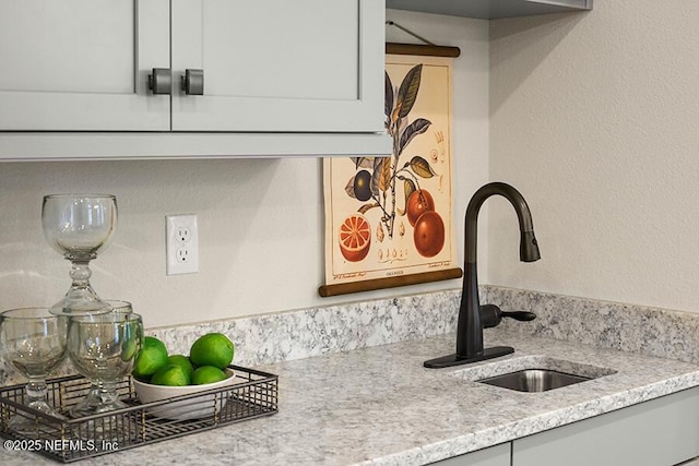 room details featuring light stone countertops, a textured wall, and a sink