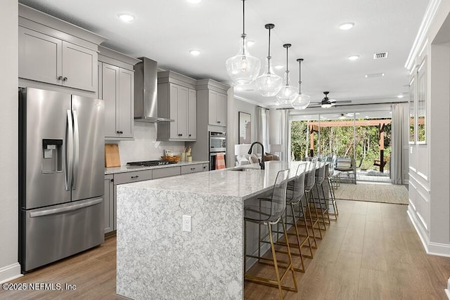 kitchen featuring a large island, gray cabinets, a sink, appliances with stainless steel finishes, and wall chimney exhaust hood