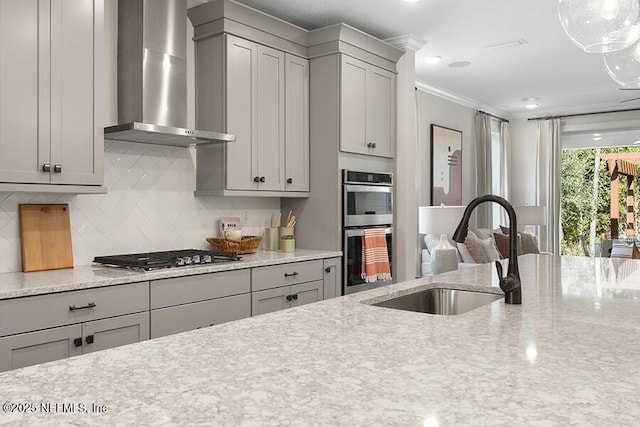 kitchen featuring gray cabinets, a sink, appliances with stainless steel finishes, wall chimney range hood, and decorative backsplash