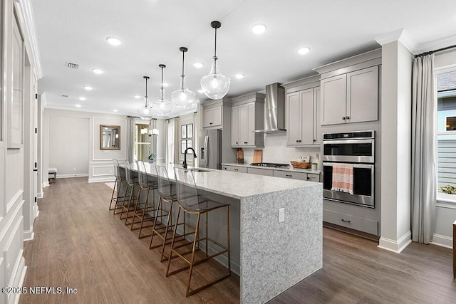 kitchen with gray cabinetry, a kitchen breakfast bar, a spacious island, stainless steel appliances, and wall chimney range hood