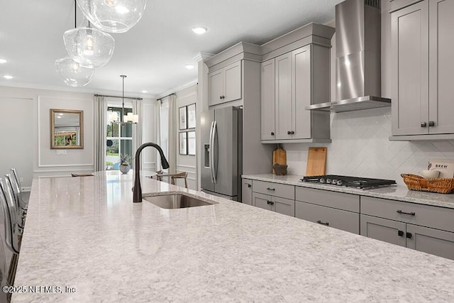 kitchen featuring wall chimney range hood, ornamental molding, gray cabinets, stainless steel appliances, and a sink