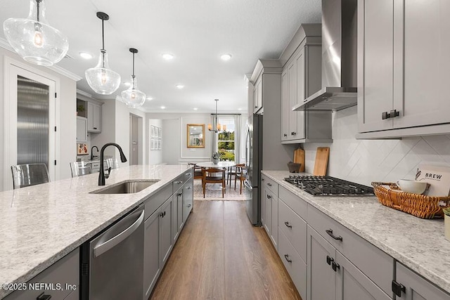 kitchen featuring gray cabinetry, appliances with stainless steel finishes, wood finished floors, wall chimney exhaust hood, and a sink