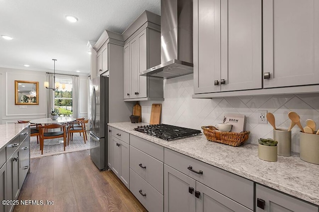 kitchen with gray cabinets, dark wood finished floors, stainless steel appliances, wall chimney range hood, and decorative backsplash