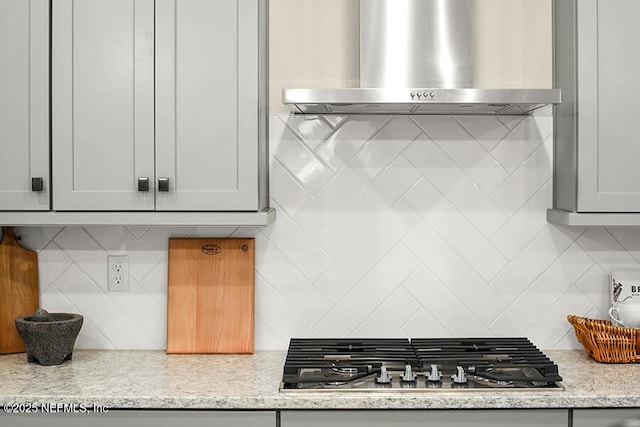 kitchen with decorative backsplash, stainless steel gas stovetop, wall chimney exhaust hood, and light stone counters