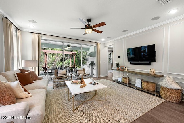 living area featuring a ceiling fan, a decorative wall, wood finished floors, and ornamental molding