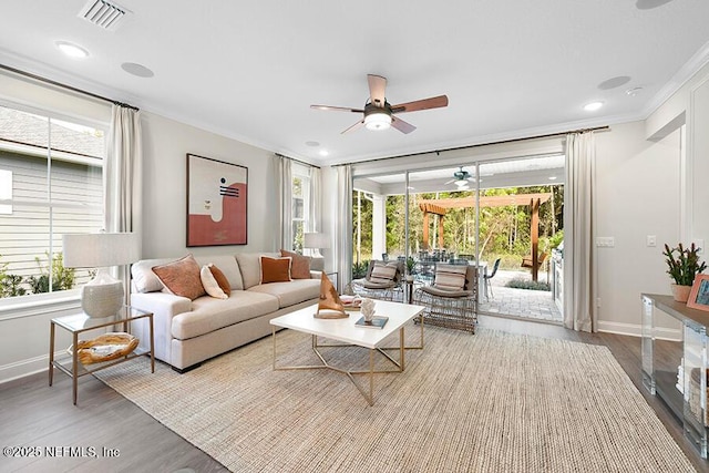 living room with visible vents, wood finished floors, crown molding, baseboards, and ceiling fan