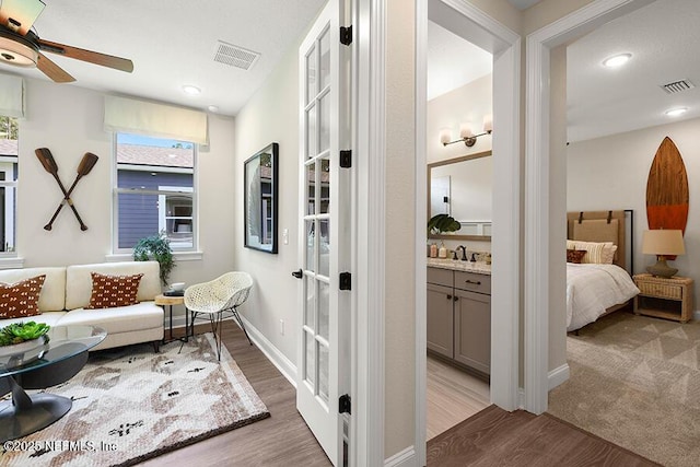 hallway with light wood-style flooring, baseboards, visible vents, and a sink