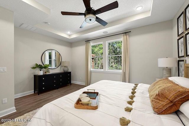 bedroom featuring a tray ceiling, wood finished floors, visible vents, and a textured ceiling