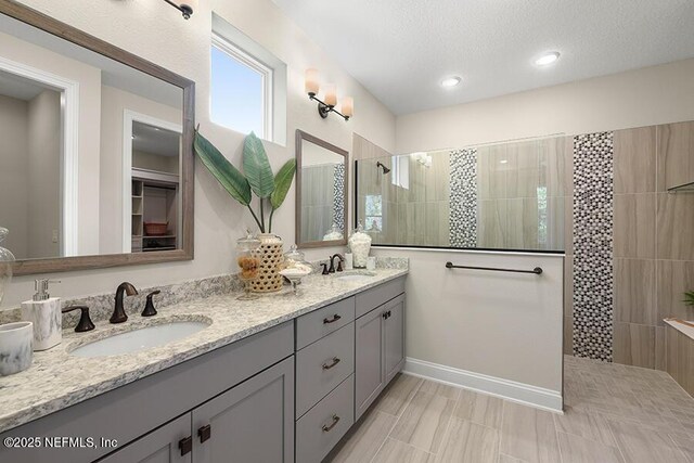 full bathroom with a textured ceiling, double vanity, a walk in shower, and a sink