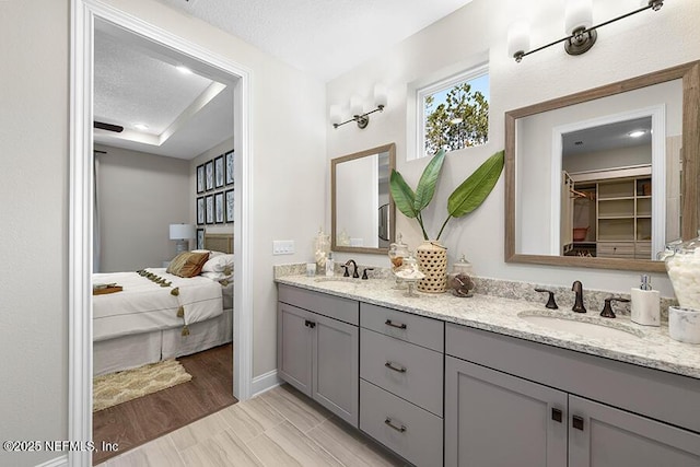 bathroom with a textured ceiling, double vanity, ensuite bathroom, and a sink